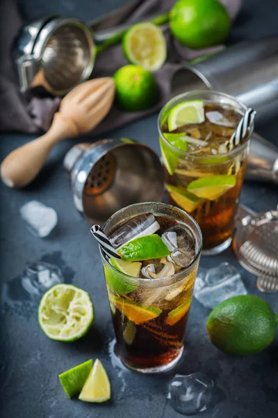 Food and drink, holidays party concept. Cuba libre or long island iced tea alcohol cocktail drink beverage, longdrink in a glass with straw, ice and lime on a dark table