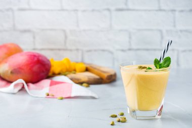 Sağlıklı organik mango lassi, güler yüzlü, sallamak, Hint içki içecek bir mutfak masasının üzerinde taze olgunlaşmış meyve ve yoğurt ile.