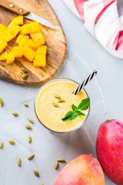 Sağlıklı organik mango lassi, güler yüzlü, sallamak, Hint içki içecek yoğurt ve mutfak masasının üzerinde taze olgunlaşmış meyve ile. Üst görüntülemek düz yatıyordu arka plan
