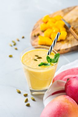 Sağlıklı organik mango lassi, güler yüzlü, sallamak, Hint içki içecek bir mutfak masasının üzerinde taze olgunlaşmış meyve ve yoğurt ile.