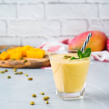 Sağlıklı organik mango lassi, güler yüzlü, sallamak, Hint içki içecek bir mutfak masasının üzerinde taze olgunlaşmış meyve ve yoğurt ile.