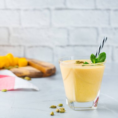 Sağlıklı organik mango lassi, güler yüzlü, sallamak, Hint içki içecek bir mutfak masasının üzerinde taze olgunlaşmış meyve ve yoğurt ile.