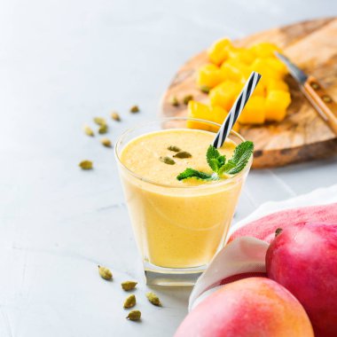 Sağlıklı organik mango lassi, güler yüzlü, sallamak, Hint içki içecek bir mutfak masasının üzerinde taze olgunlaşmış meyve ve yoğurt ile.