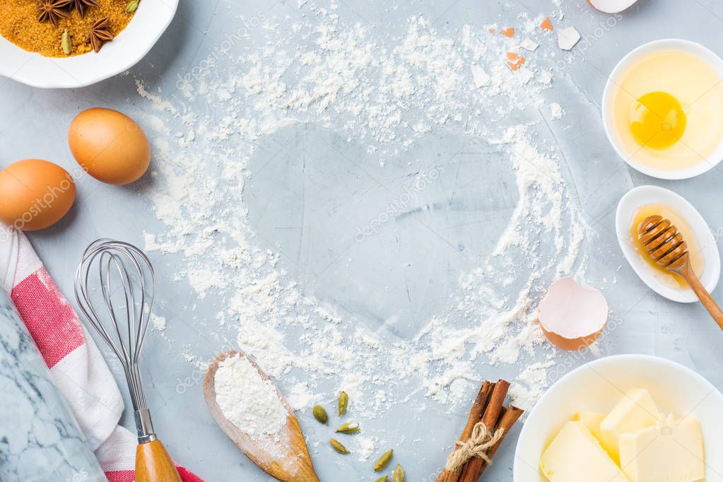 Baking cooking ingredients and utensils with heart shaped frame for valentines day on a kitchen table. Flour, sugar, butter, eggs, spices, honey. Top view flat lay copy space background