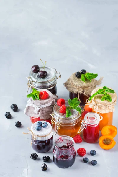 Food and drink, harvest summer autumn concept. Assortment of seasonal berries and fruits jams in jars on a wooden table. Copy space rustic background