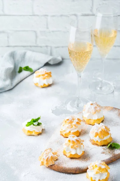 Food and drink, holidays concept. Delicious sweet homemade profiteroles with cream and glasses of champagne on a modern kitchen table