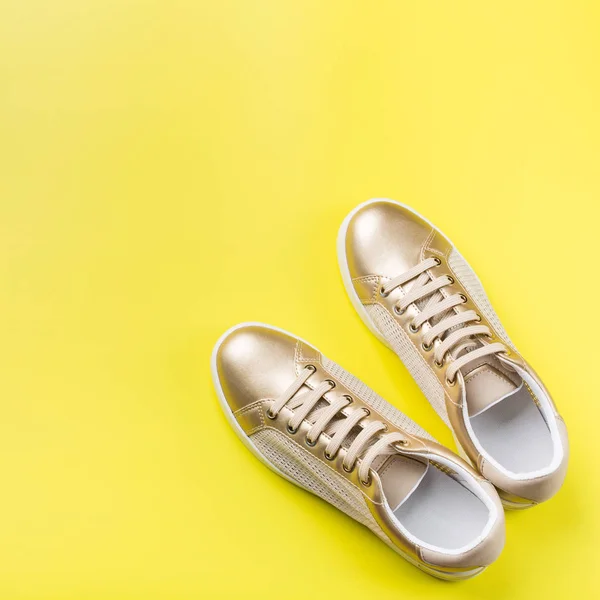 Pair of golden female sneakers on yellow background — Stock Photo, Image