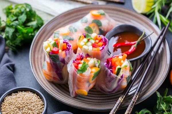 Spring or summer rolls with rice paper, carrot, chili sauce, red cabbage, zucchini , pepper, shrimps and kumquats. Tasty asian food.