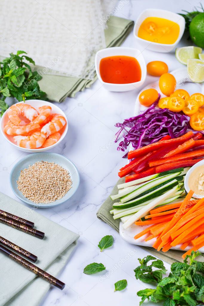 Spring or summer rolls preparation with rice paper, carrot, chili sauce, red cabbage, zucchini , pepper, shrimps and kumquats. Tasty asian food.