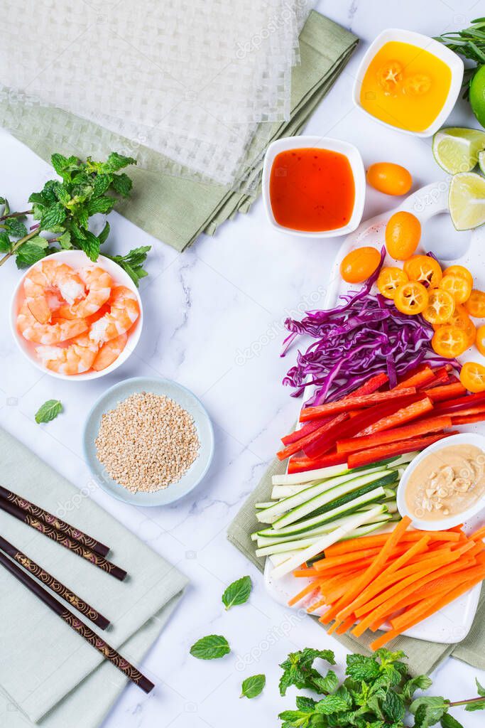 Spring or summer rolls preparation with rice paper, carrot, chili sauce, red cabbage, zucchini , pepper, shrimps and kumquats. Tasty asian food. Flat lay top view background 