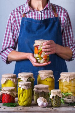 Ev yapımı ve mayalanmış yiyeceklerle dolu kavanozda el ele tutuşan olgun bir kadın. Türlü çeşit salamura ve marine edilmiş sebze. Oda temizliği, ev ekonomisi, hasat koruma  