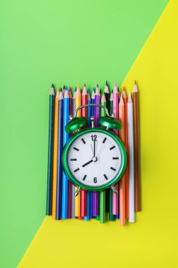 Nane yeşili ve sarı arka planda renkli gökkuşağı kalemleri ve çalar saat çeşitleri. En üstteki düz yerde. Okul konseptine dönelim.