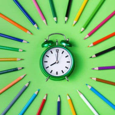 Nane yeşili arka planda renkli gökkuşağı kalemleri ve çalar saat çeşitleri. En üstteki düz yerde. Okul konseptine dönelim.