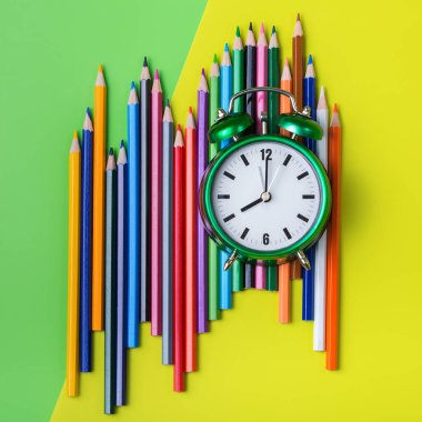 Nane yeşili ve sarı arka planda renkli gökkuşağı kalemleri ve çalar saat çeşitleri. En üstteki düz yerde. Okul konseptine dönelim.