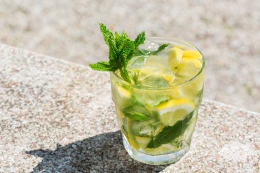 Masada rom, limon, nane ve buz ile klasik kokteyl mojito. Yaz ferahlatıcı içecek güneşli, canlı, sert ışık ve gölgelerle, açık havada.