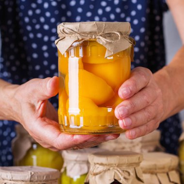 Ev yapımı ve mayalanmış yiyeceklerle dolu kavanozda el ele tutuşan olgun bir kadın. Çeşitli sebze turşusu ve marine edilmiş sebzeler, meyve kompostosu. Oda temizliği, ev ekonomisi, hasat koruma  