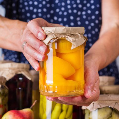 Ev yapımı ve mayalanmış yiyeceklerle dolu kavanozda el ele tutuşan olgun bir kadın. Çeşitli sebze turşusu ve marine edilmiş sebzeler, meyve kompostosu. Oda temizliği, ev ekonomisi, hasat koruma  