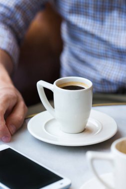 Genç başarılı iş adamı bir kafede oturuyor, sabah kahvesini içiyor ve akıllı telefon kullanıyor. Doğal ışık ile yaşam biçimi bileşimi 