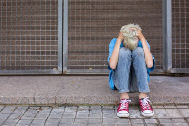 A Sad Lonely teenager hiding his face and crying while sitting alone on the floor outdoors. Young boy struggling with inner problems. Homelessness, Loneliness, bullying, depression and sadness concept