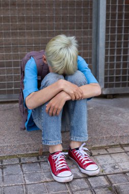 A Sad Lonely teenager hiding his face and crying while sitting alone on the floor outdoors. Young boy struggling with inner problems. Homelessness, Loneliness, bullying, depression and sadness concept