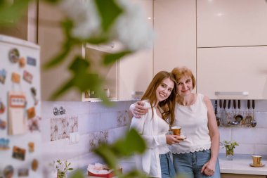 .Elinde kahve, elinde çay, elinde altın bardakla, annenle baş başa duran, kameraya bakan bir kız..