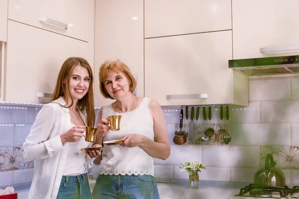 Las mujeres sostienen tazas de oro con café, té en las manos disfrutando de la conversación, mirando en la cámara —  Fotos de Stock