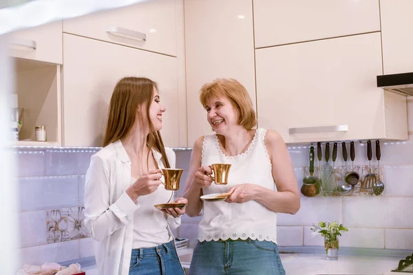 Retrato de una madre y una hija ancianas felices en el interior de la cocina moderna y luminosa riéndose y mirándose unos a otros —  Fotos de Stock