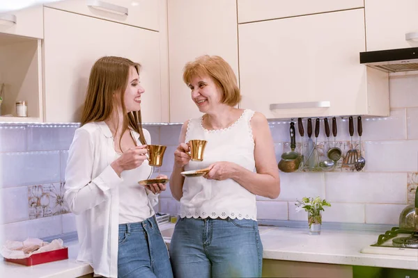 Retrato de una madre y una hija ancianas felices en el interior de la cocina moderna y luminosa, mirándose entre sí —  Fotos de Stock