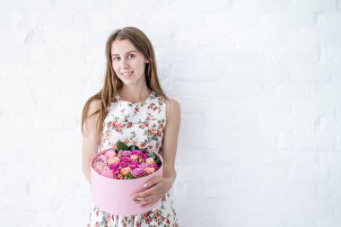 Kız, elinde pembe çiçekler, pembe güller ve Fransız kurabiyeleriyle dolu büyük yuvarlak bir kutu tutuyor. Kadın, anneler günü, sevgililer günü, kadınlar günü, doğum günü hediyesi alıyor. Çiçekçiyi kapat..