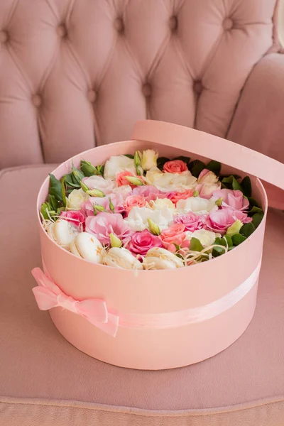 Close up of round pink box with ribbon and flowers,french macarons inside and top on armchair.Romantic bouquet,floral composition of rose,eustoma.Florist make wedding decor.Present for valentine day
