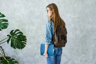 Kahverengi sırt çantası ve kitaplarla gülümseyen beyaz kız.