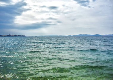 Küçük kasaba ve dağların manzarası ile dalgalı denizde bulutlu bir gün