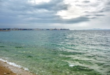 Deniz dalgaları ve arka planda bir kasaba ile bulutlu bir gün.