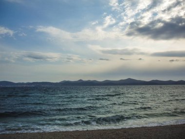 Arka planda dağlar ile çakıl plaj dalgalar deniz.