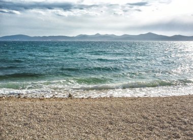 Dalgalar ve çakıl plajı ile arka planda dağlar denize sıfır.