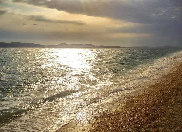 Parlak gün batımı, deniz dalgaları ve çakıl plajı.
