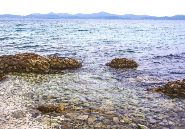 Καθαρά Μικρά Κύματα Θαλάσσης Βράχια Και Βουνά Στο Παρασκήνιο — Φωτογραφία Αρχείου