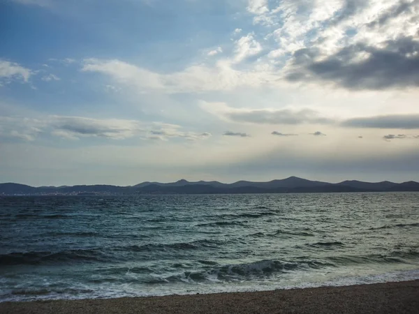 Arka planda dağlar ile çakıl plaj dalgalar deniz.