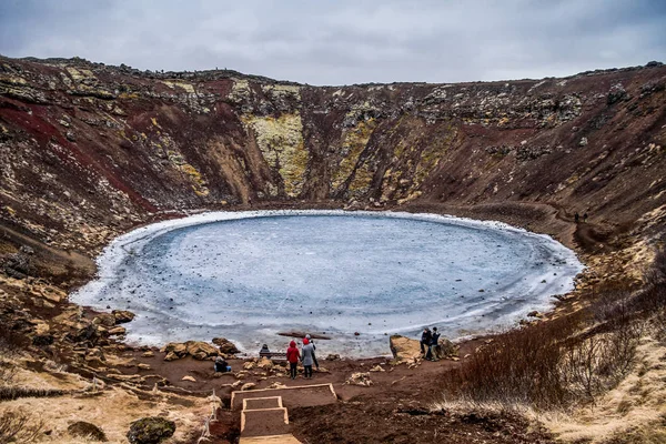 Kerid volcanic crater and its blue pond, Golden Circle, Iceland. The winter colours of beautiful Kerio, or Kerid crater in western Iceland. Red volcanic rock, green mossy slopes and a circle of breaking ice in a turquoise lake.