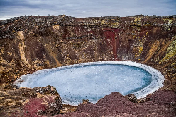 Kerid volcanic crater and its blue pond, Golden Circle, Iceland. The winter colours of beautiful Kerio, or Kerid crater in western Iceland. Red volcanic rock, green mossy slopes and a circle of breaking ice in a turquoise lake.