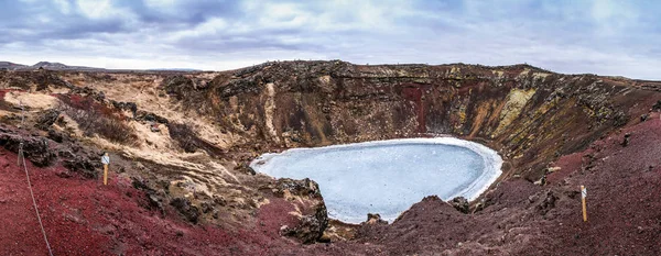 Kerid volcanic crater and its blue pond, Golden Circle, Iceland. The winter colours of beautiful Kerio, or Kerid crater in western Iceland. Red volcanic rock, green mossy slopes and a circle of breaking ice in a turquoise lake.