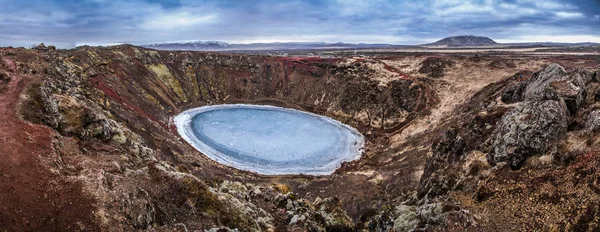 Kerid volcanic crater and its blue pond, Golden Circle, Iceland. The winter colours of beautiful Kerio, or Kerid crater in western Iceland. Red volcanic rock, green mossy slopes and a circle of breaking ice in a turquoise lake.