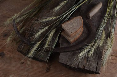 Ekmek, buğday kulakları ve ahşap bir tahtanın üzerinde eski bir orak. Bir avuç biçilmiş buğday kulağı ve el yapımı Orakçı kancası sapığı.