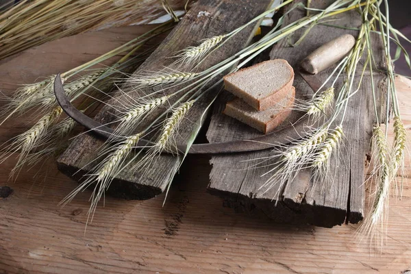 Ekmek, buğday kulakları ve ahşap bir tahtanın üzerinde eski bir orak. Bir avuç biçilmiş buğday kulağı ve el yapımı Orakçı kancası sapığı.