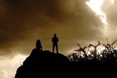 epik bir gökyüzü ile bir dağın tepesinde siluetleri