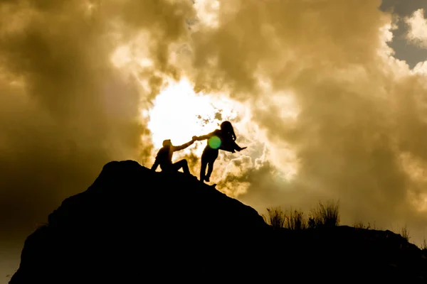 silhouettes on top of a mountain with an epic sky