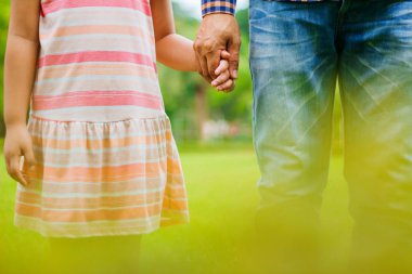 Çimenlerin üzerinde duran küçük bir kız, iki yükselterek doğal bir arka plan üzerinde eller.