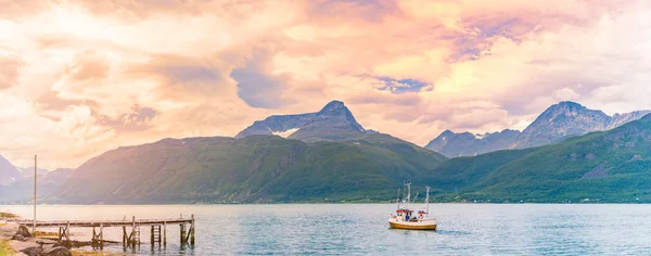Tugboat or fishing boat at sunset in Norway, Europe. Ship in foreground and blue sky and mountains in background. Scandinavia travel.
