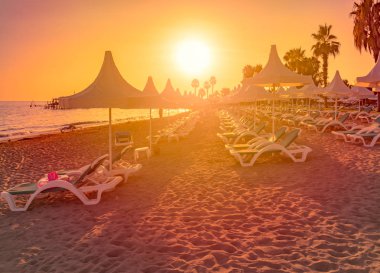 Güneşin altında arka plan ile ön plan, beyaz gölge şemsiyeleri ve turuncu günbatımı gökyüzü kum ile Türkiye'deki Beach