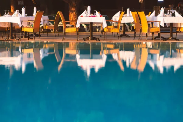 Chairs and table near pool at hotel restaurant. Cutlery and napkings on tables. Resort life on holidays.